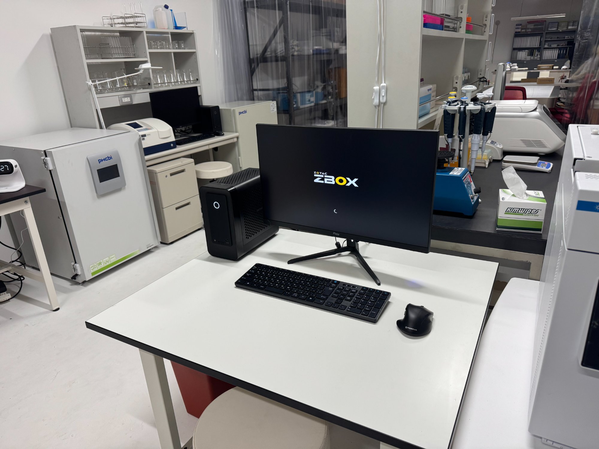 科捜研ラボセットのデスクに設置されたZOTAC ZBOX MAGNUS ONE。モニターにZBOXロゴが表示されている。